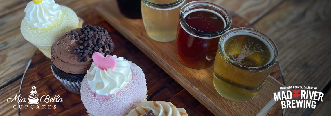A wooden tray with cupcakes and flight of beer