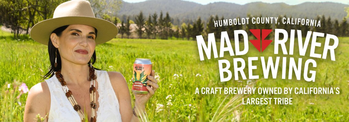 Maize Goddess MRB Press Release Cover Image Linda Cooley, CEO holds up can of new Maize Goddess Indigenous Ale against a backdrop of tall grass and trees in the distance.